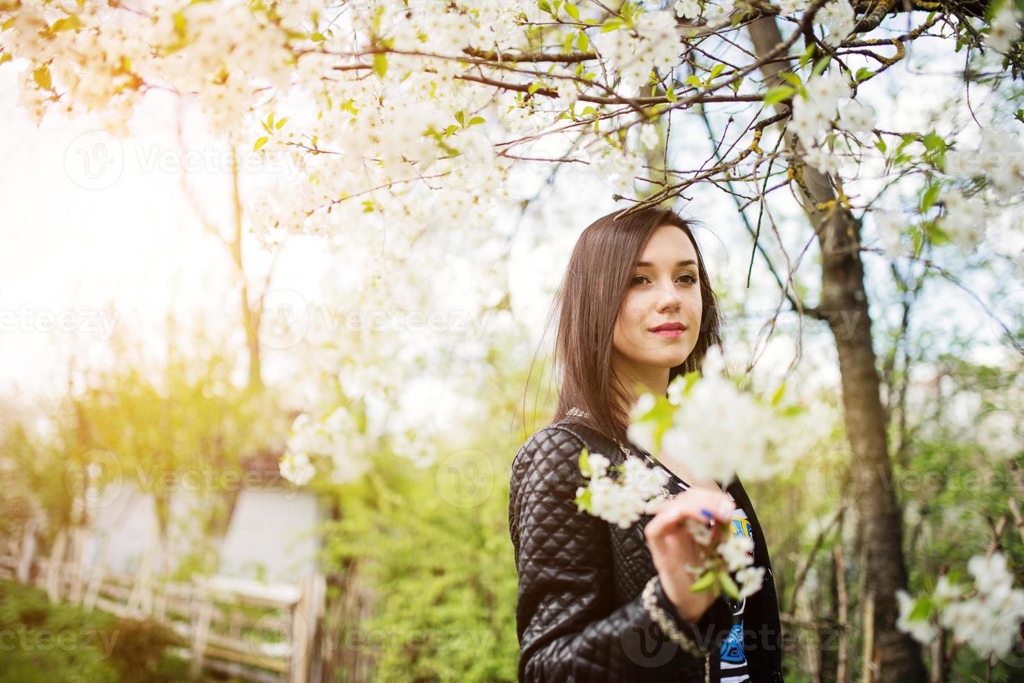 Cierra el retrato de una joven morena con flor de cerezo en el jardín de primavera. foto