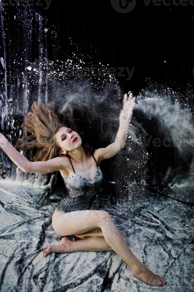 Girl dancer jumping and dancing in the white dust with flour on a black background. Studio shot of woman dancing with flour. photo
