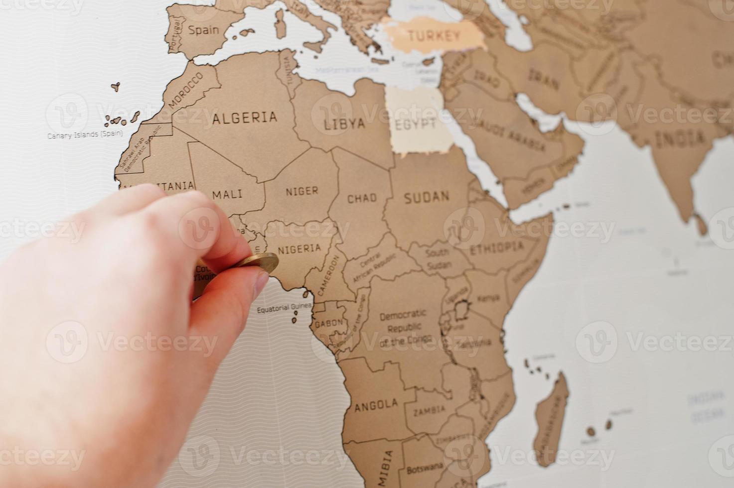 Scratch travel map of the world. Scratch travel map of the world. Hand of man erase Africa Nigeria with coin. photo