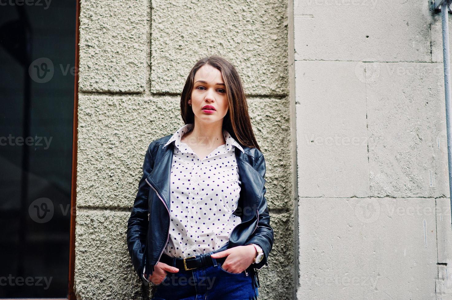 retrato de una joven elegante vestida con una chaqueta de cuero y jeans rotos en las calles de la ciudad. estilo de modelo de moda callejera. foto