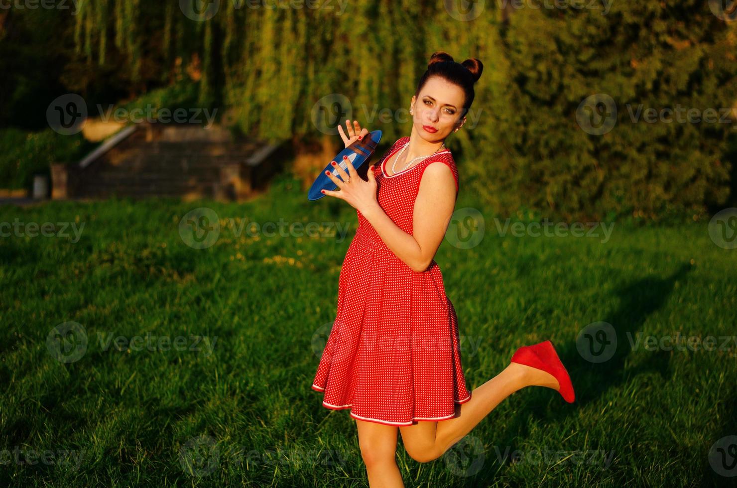 Portrait of young pinup girl wearing at retro vintage old-fashioned dress in peas with vinyl audio record, retro styling. photo