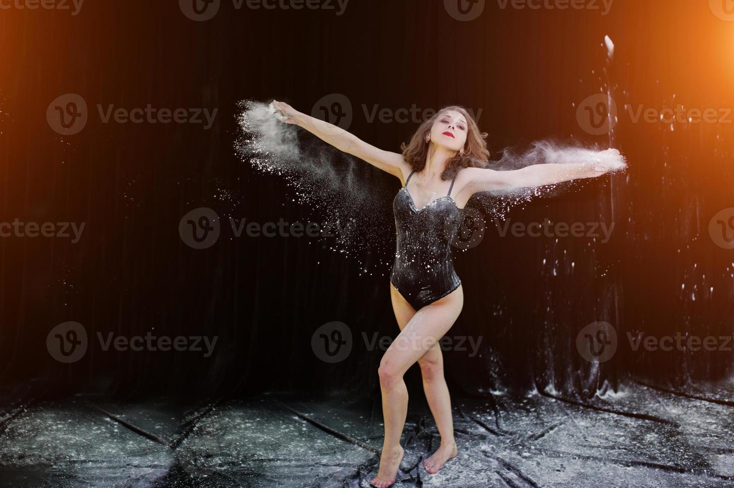 Girl dancer jumping and dancing in the white dust with flour on a black background. Studio shot of woman dancing with flour. photo