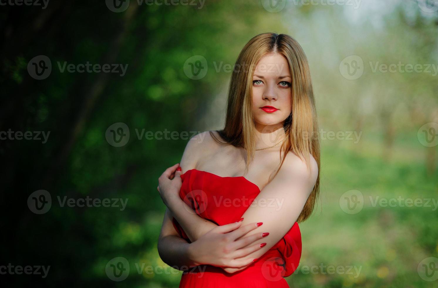 Portrait of light hair girl on red dress background spring garden. photo
