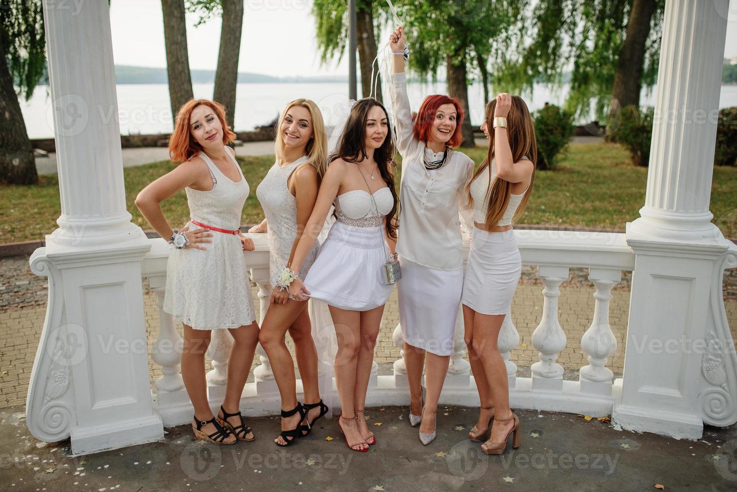 Five girls with balloons at hand weared on white dresses on hen party against white columns of arch. photo