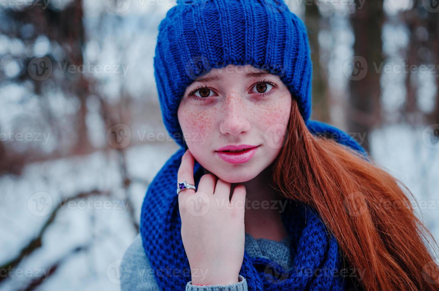 Close up portrait of young red hair girl with freckles wearing at blue knitted wool hat and scarf in winter day. photo