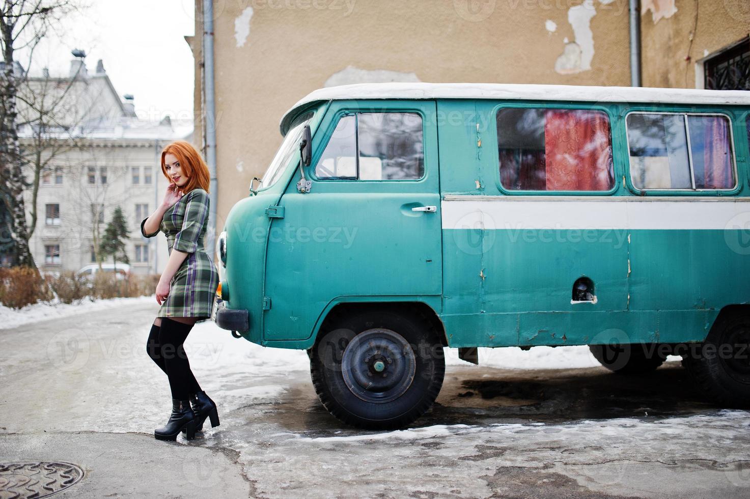 Young red haired girl posed on checkered dress background old retro cyan minivan. photo