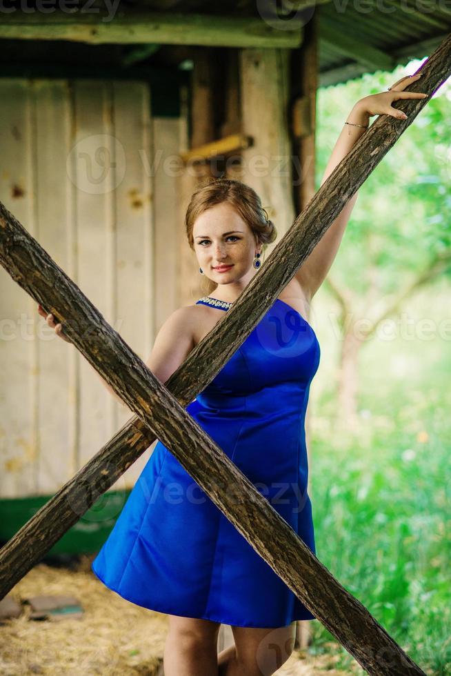 joven con sobrepeso en vestido azul plantea jardín de primavera de fondo en cabaña de madera. foto