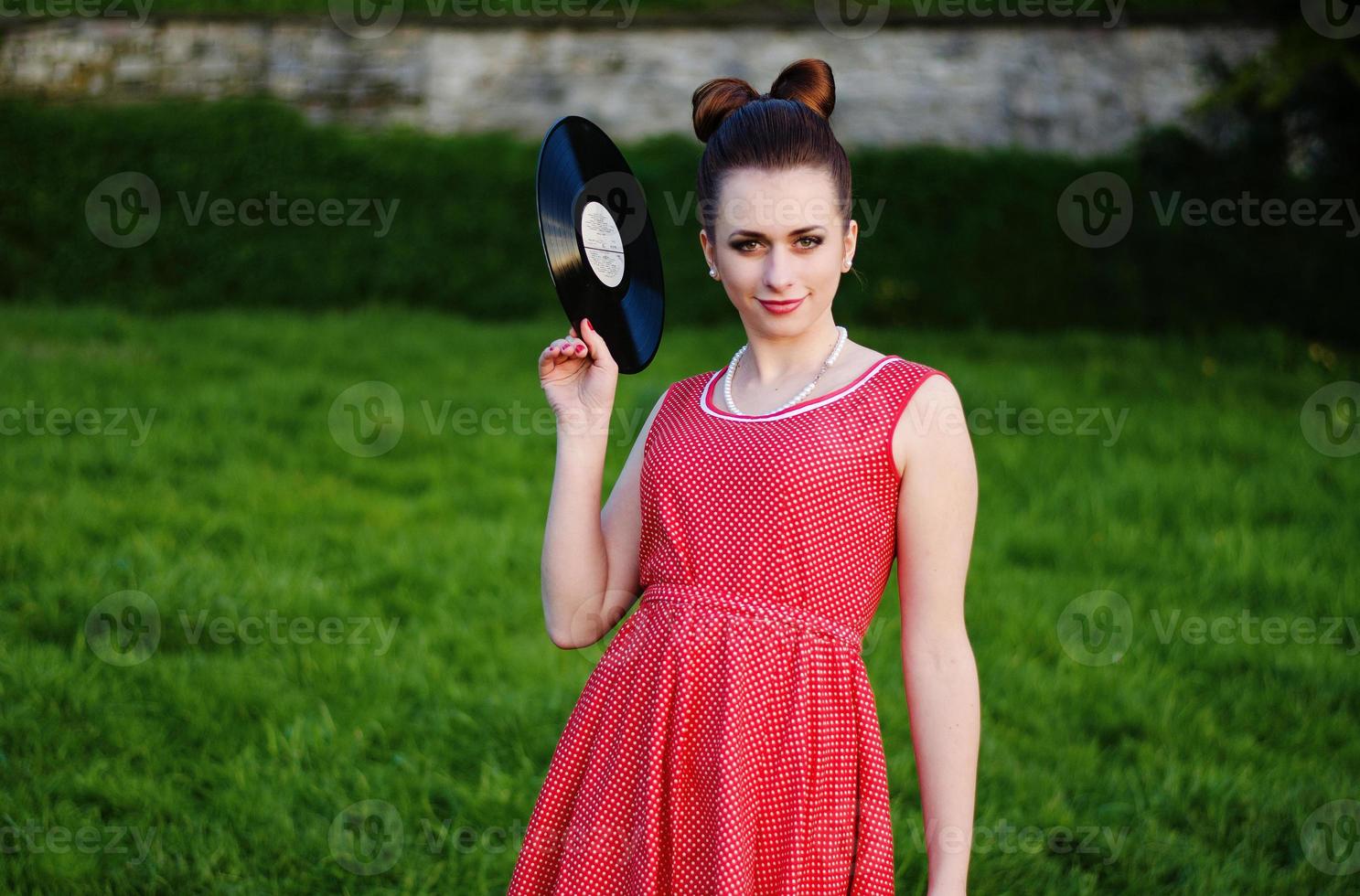 Portrait of young pinup girl wearing at retro vintage old-fashioned dress in peas with vinyl audio record, retro styling. photo