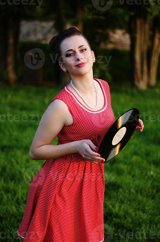 Portrait of young pinup girl wearing at retro vintage old-fashioned dress in peas with vinyl audio record, retro styling. photo