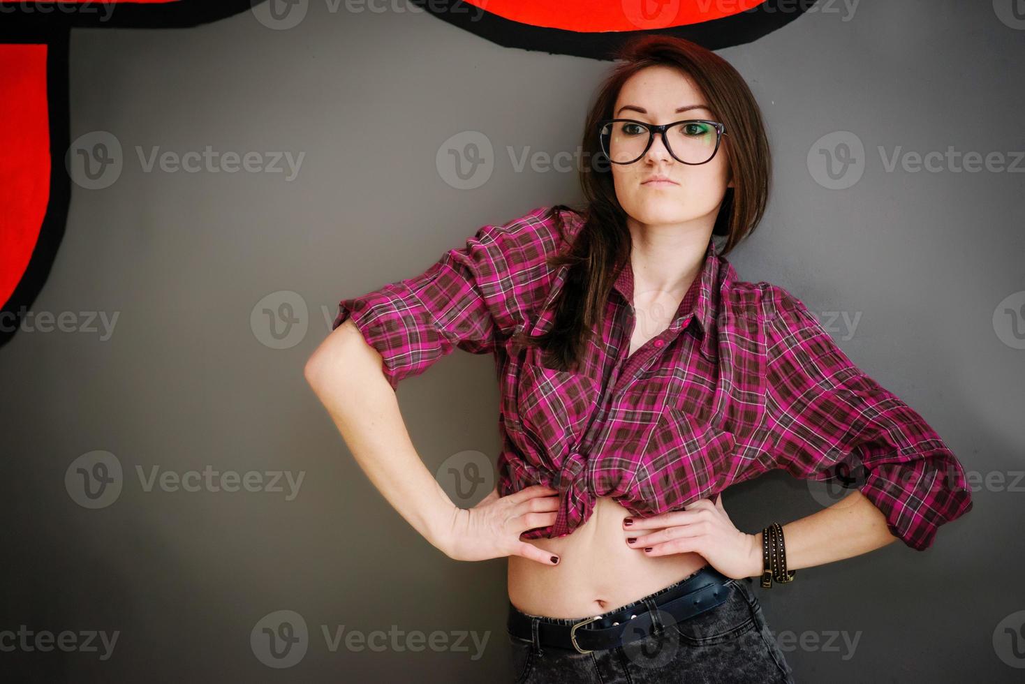 Portrait of brunette girl on glasses wearing casual clothes background gray wall with some graffity. photo