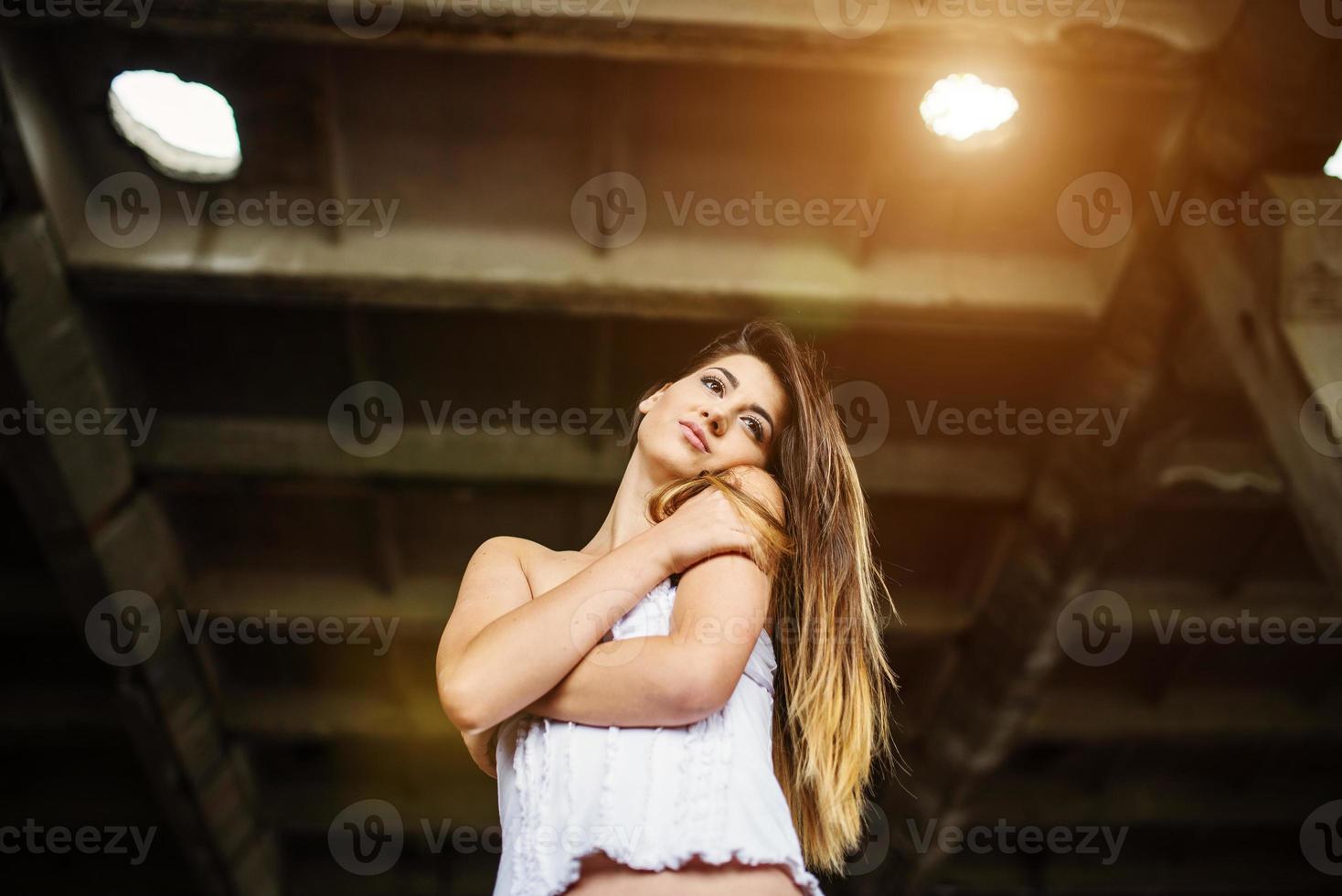 Portrait of young cute brunette girl wearing on black leather pants and white blouse posed on abandoned place. photo