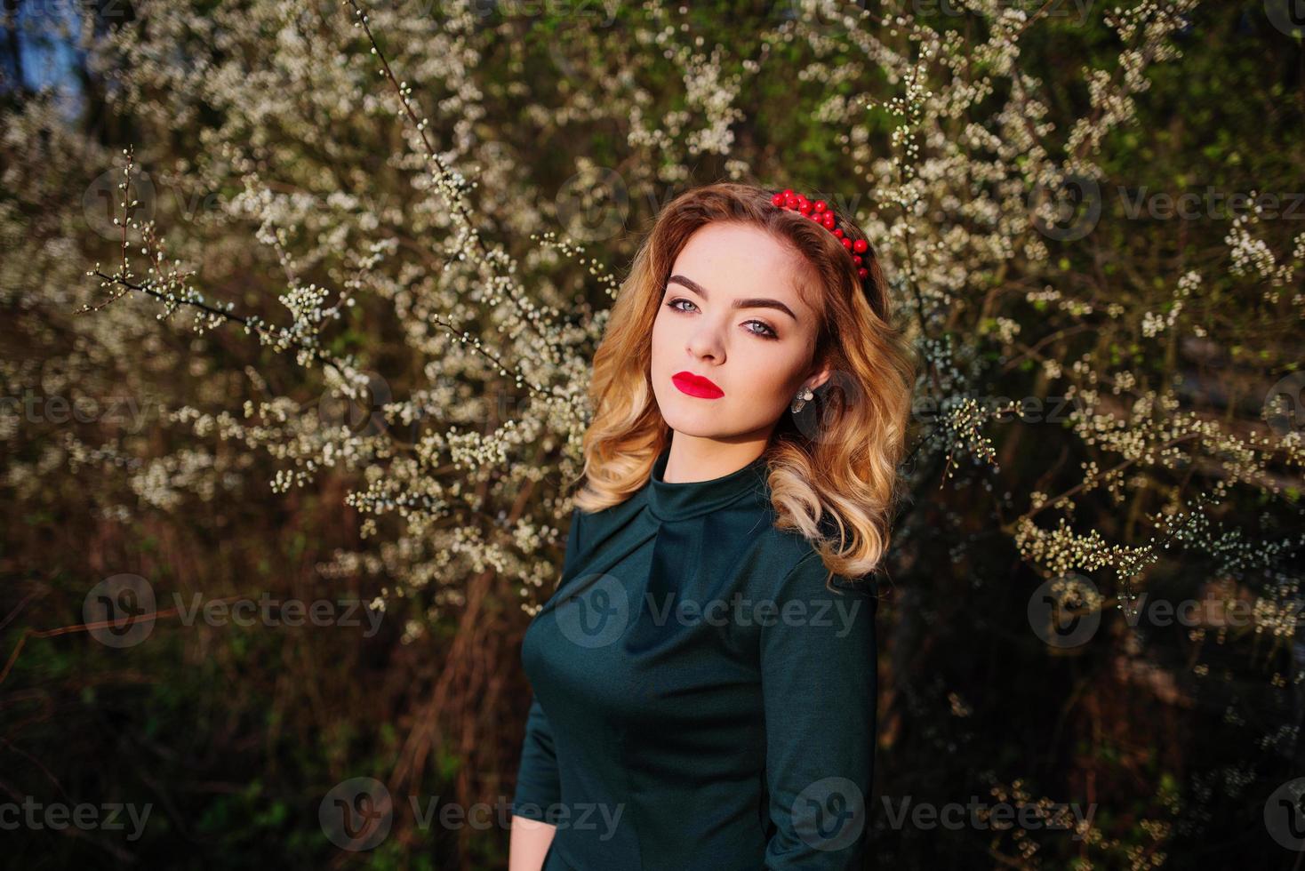 Close up portrait of yong elegance blonde girl at green dress on the garden in spring on blossom trees. photo
