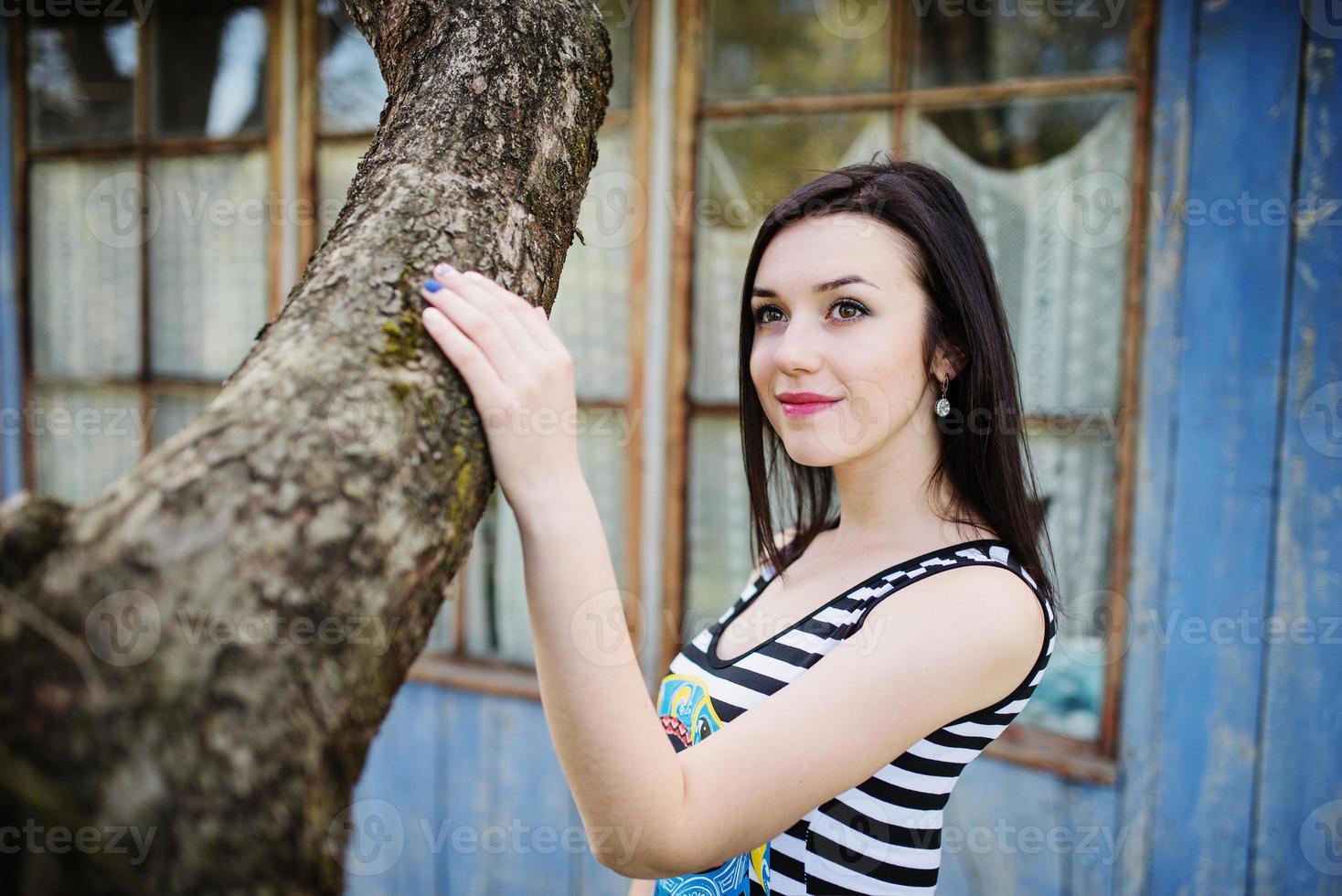 chica modelo morena en vestido con rayas planteadas cerca del árbol. foto