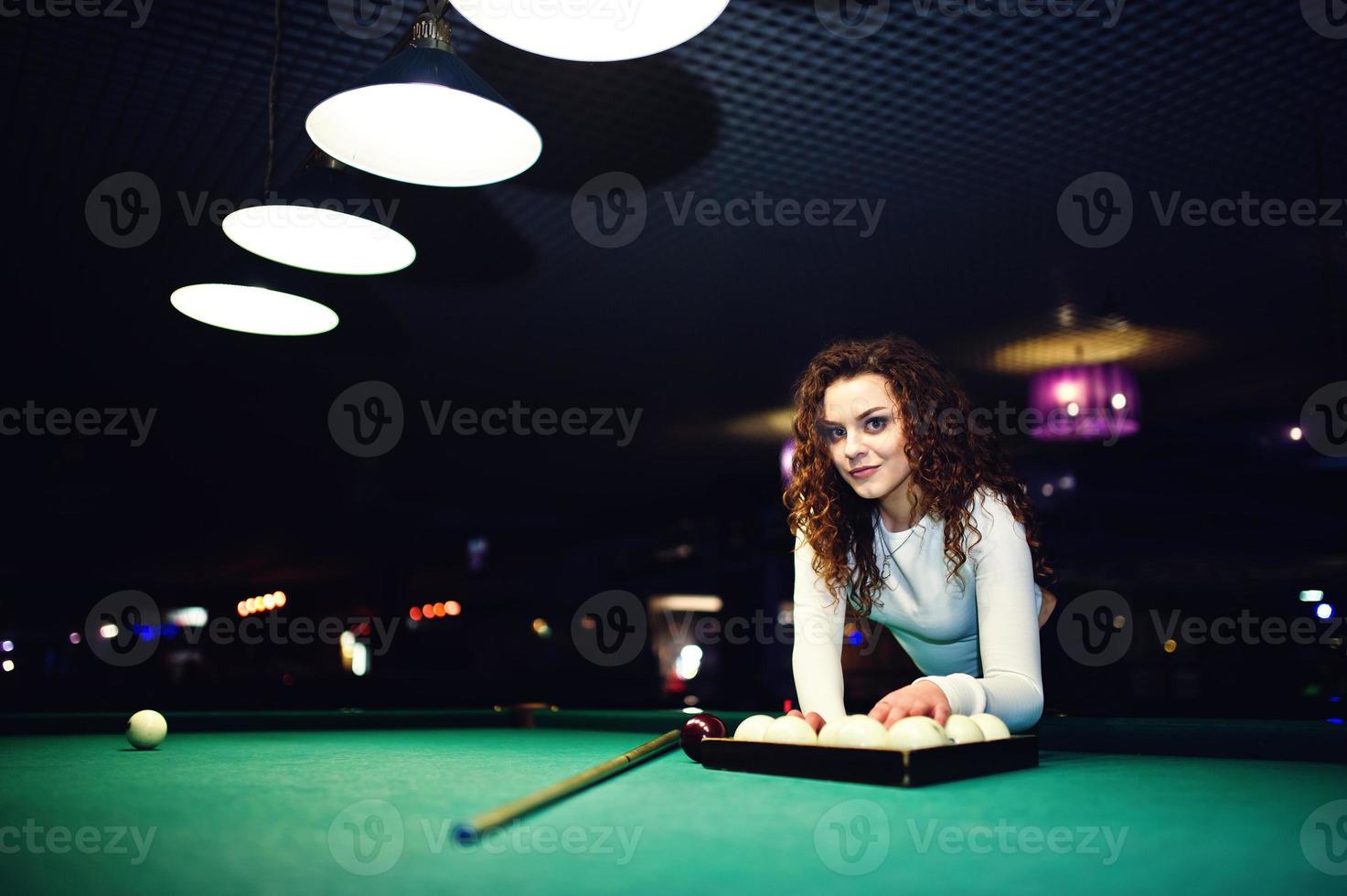 Young curly girl posed near billiard table. Sexy model at black mini mini skirt play russian snooker. Play game and fun concept. photo
