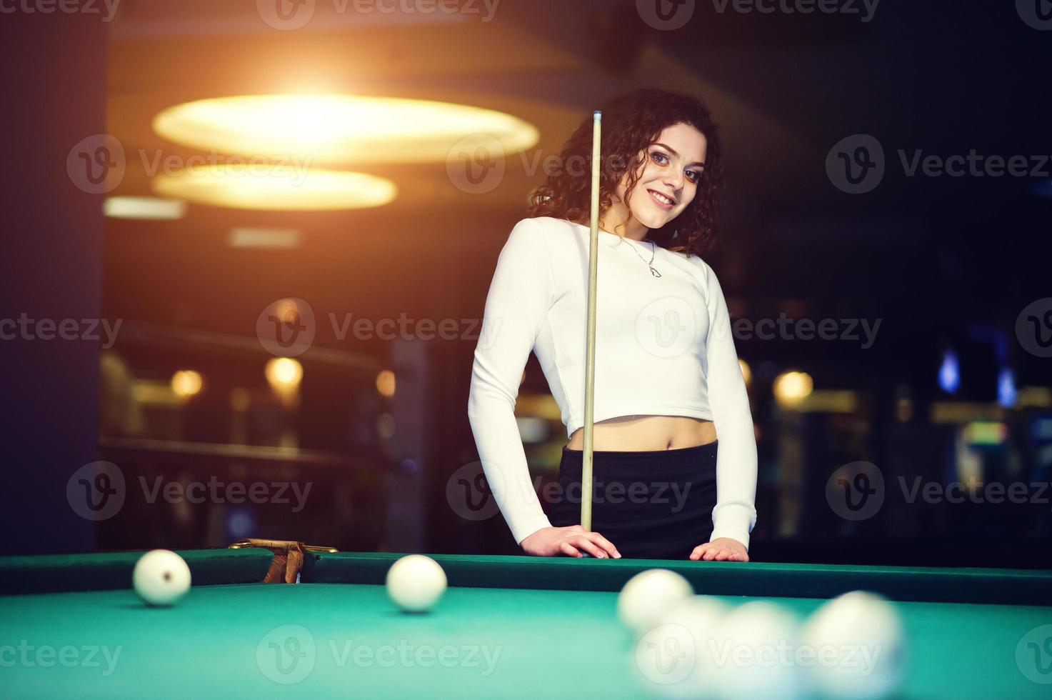 Young curly girl posed near billiard table. Sexy model at black mini mini skirt play russian snooker. Play game and fun concept. photo