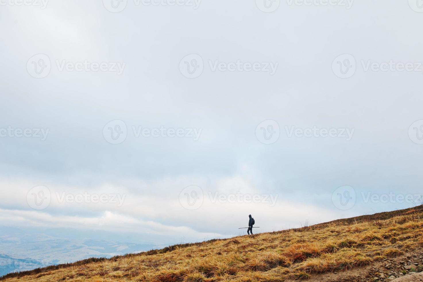 Man with a back pack walking down the mountain with stick at hand. photo