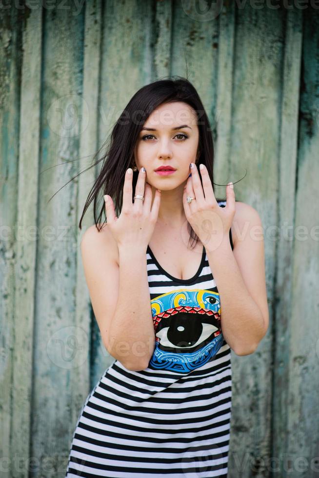 Brunette model girl at dress with stripes background cian wooden background. photo