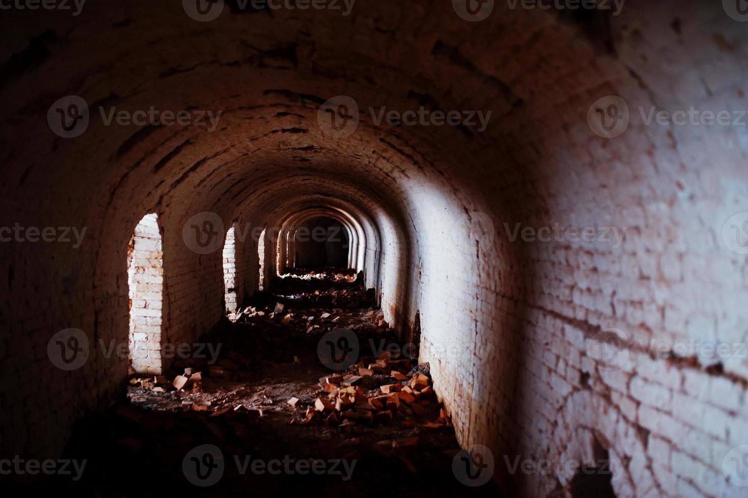 túnel de arco de ladrillo aterrador en la oscuridad y algo de luz. foto