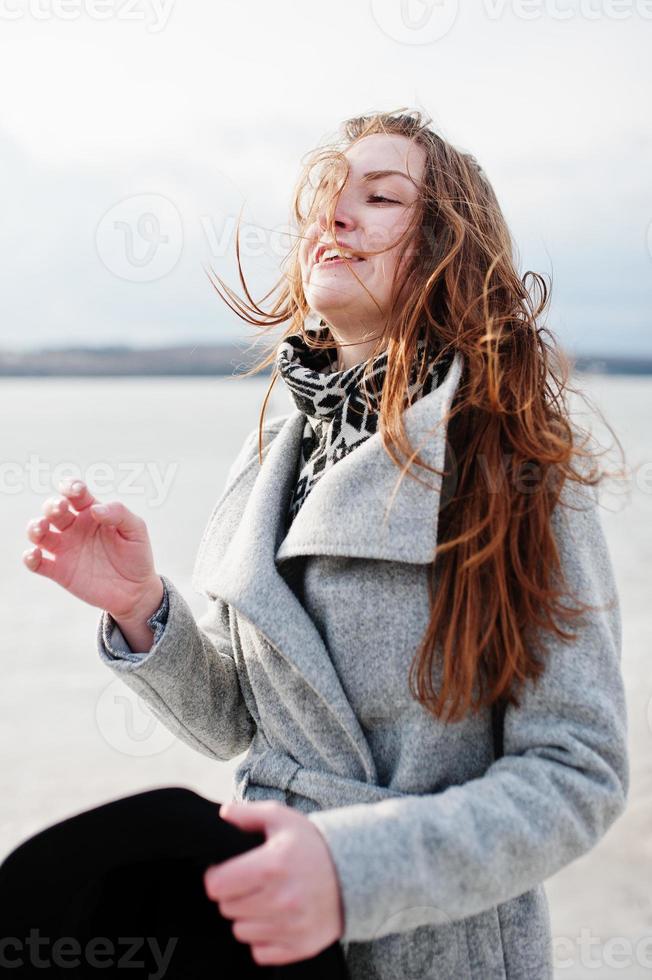 Happy funny model girl on gray coat with black hat on hand. photo