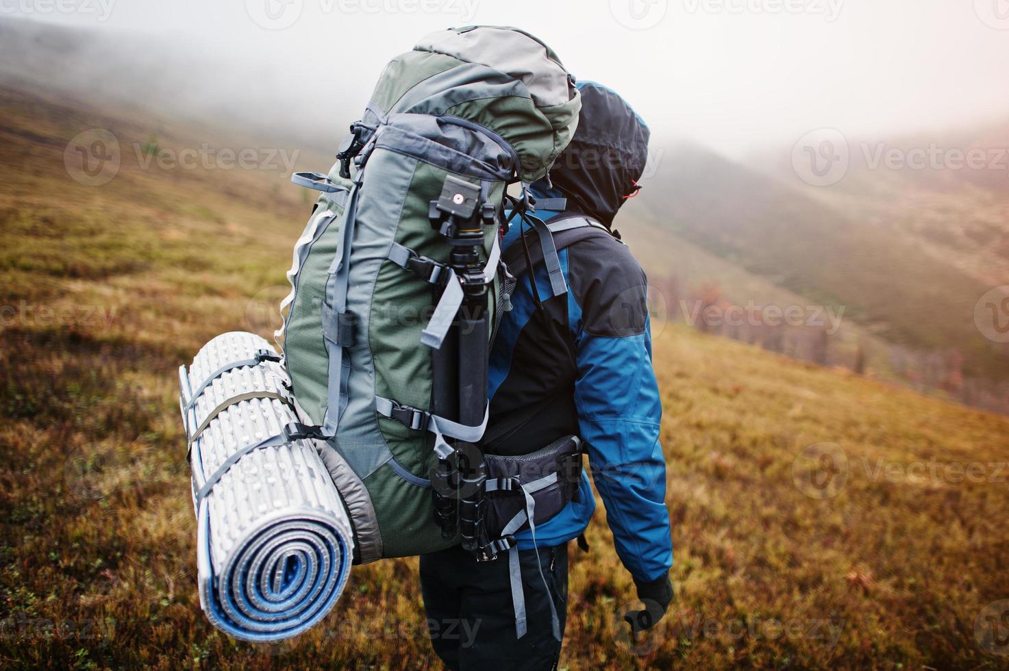 vista de cerca de las esteras y el trípode de la mochila turística trasera, vistiendo una chaqueta de turismo azul con capucha y de pie en la montaña foto