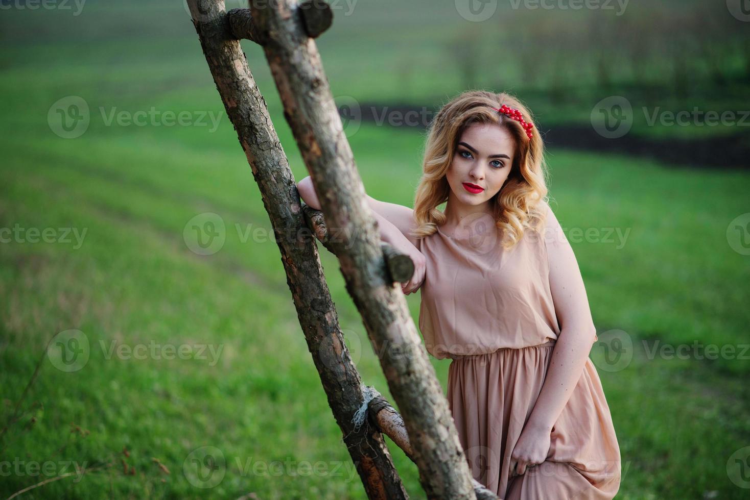 yong elegancia chica rubia en vestido de rosa en la escalera de madera de fondo de jardín. foto