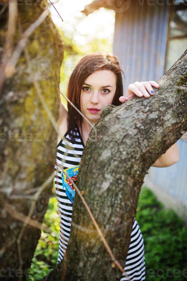 chica modelo morena en vestido con rayas planteadas cerca del árbol. foto