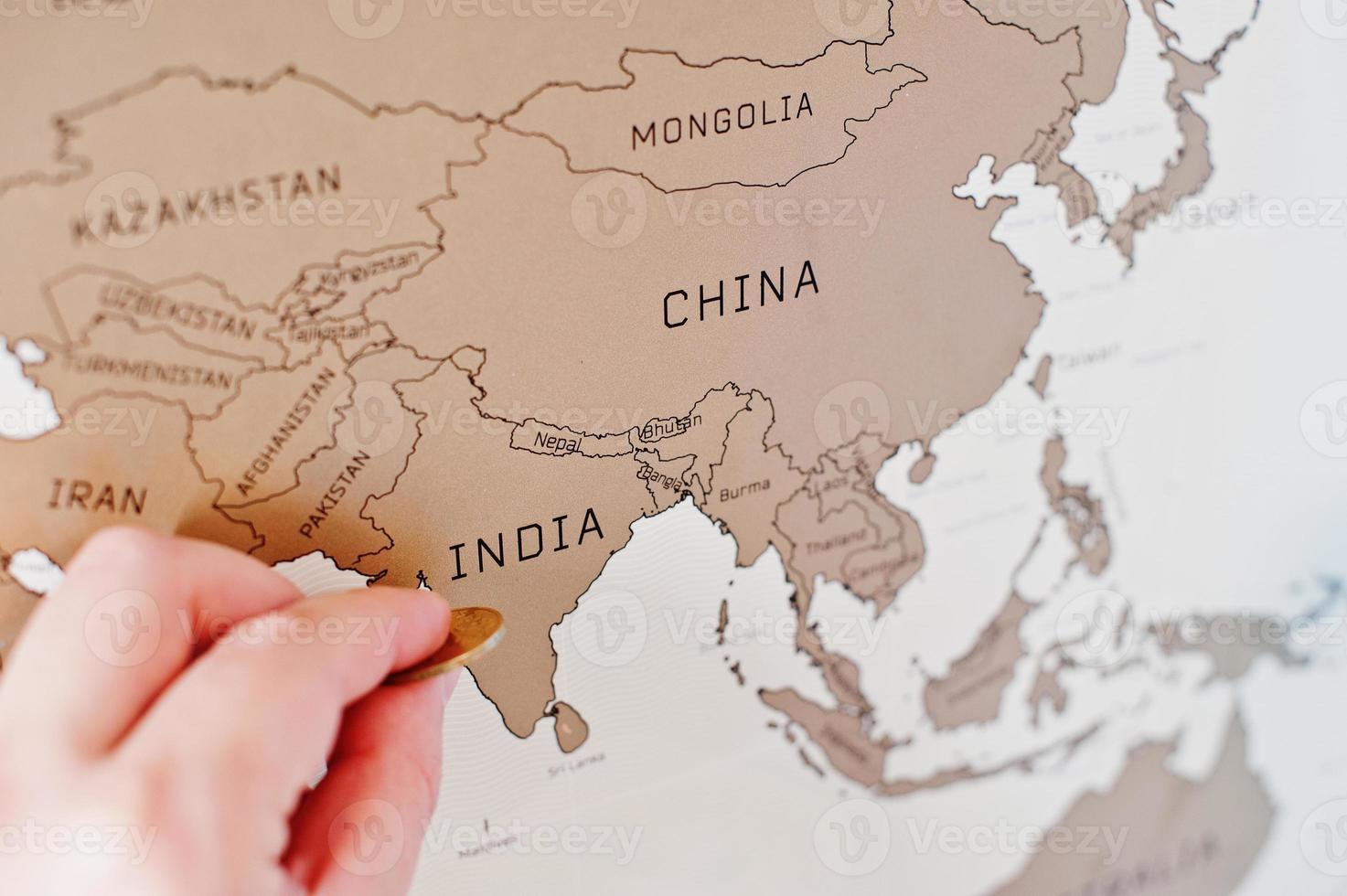 Scratch travel map of the world. Hand of man erase India with coin. photo