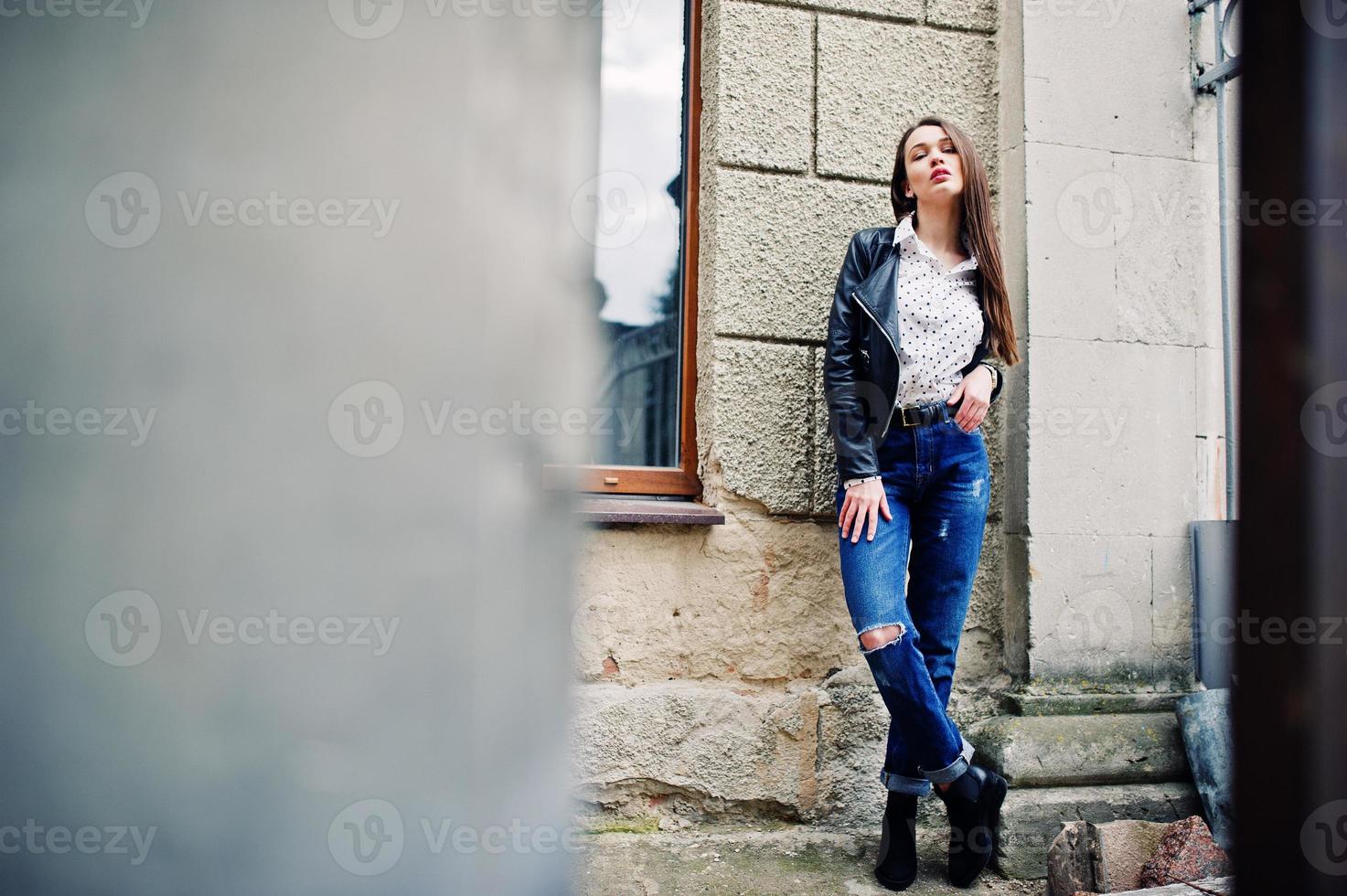 retrato de una joven elegante vestida con una chaqueta de cuero y jeans rotos en las calles de la ciudad. estilo de modelo de moda callejera. foto
