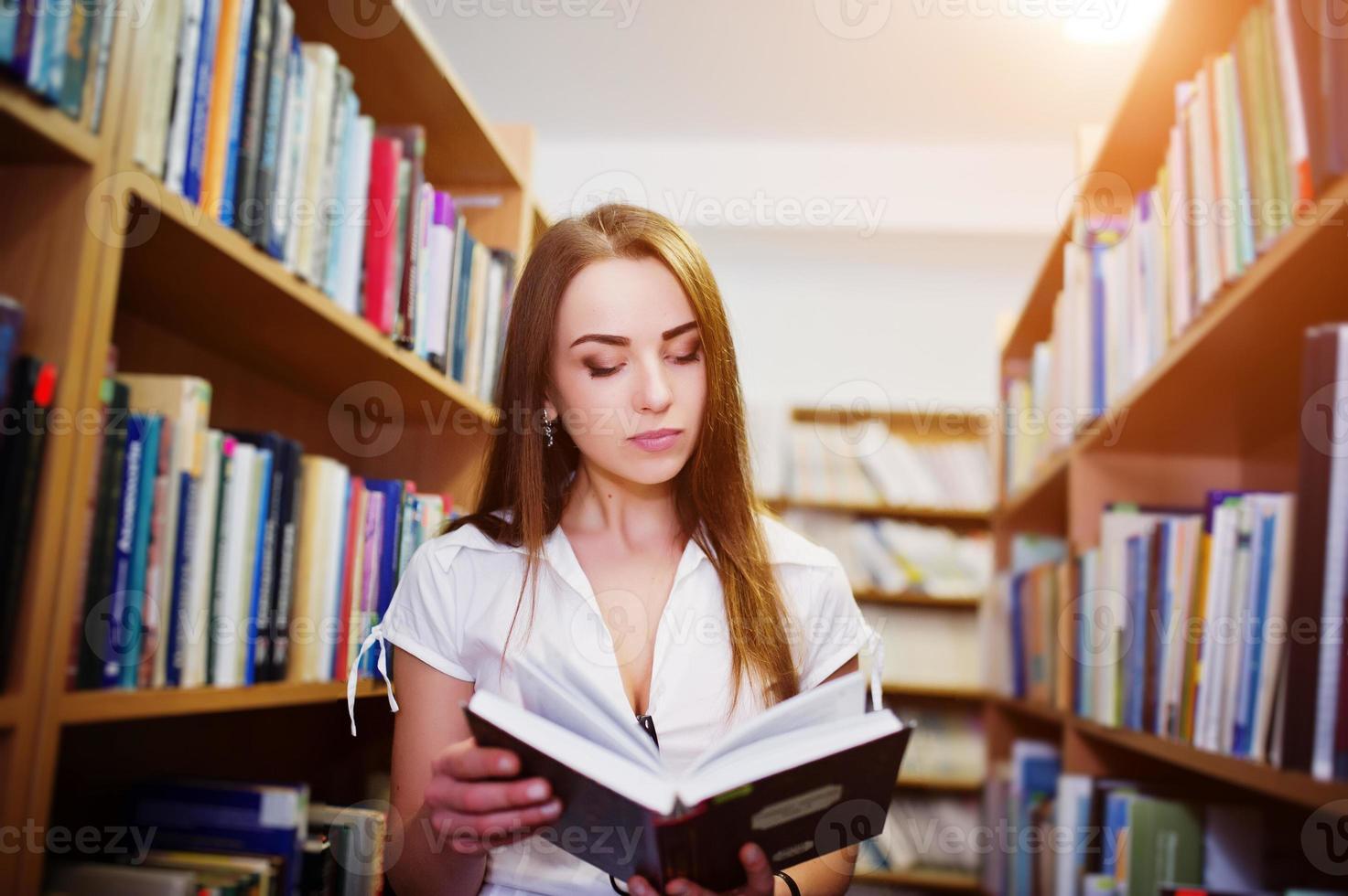 Brunette girl at library read a book, wear on white blouse and black mini skirt. Sexy business woman or teacher concept. photo