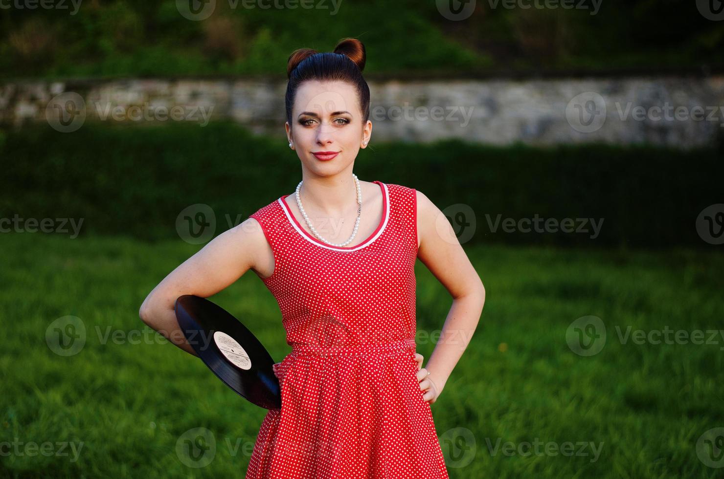 Portrait of young pinup girl wearing at retro vintage old-fashioned dress in peas with vinyl audio record, retro styling. photo