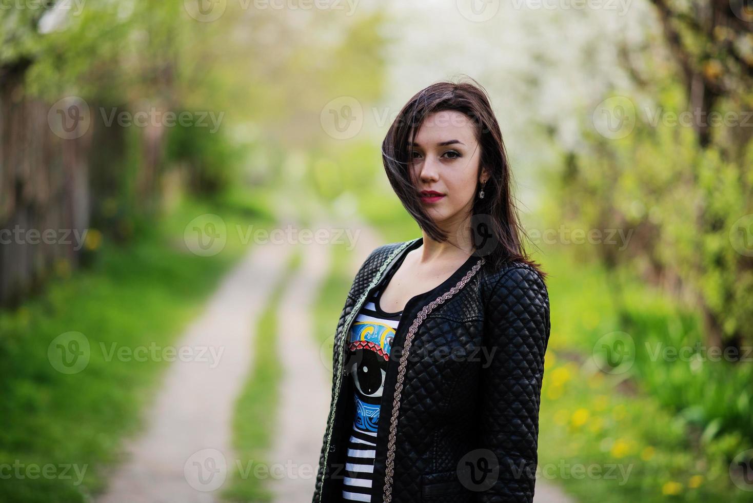 chica morena con chaqueta de cuero posada en el jardín de primavera. foto