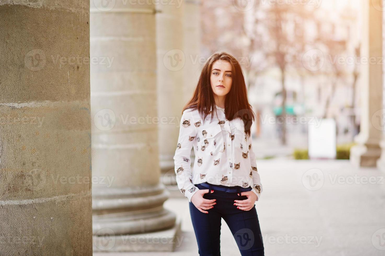 Young stylish brunette girl on shirt and pants posed near stone columns. Street fashion model concept. photo