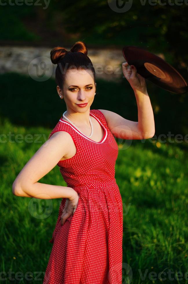 retrato de una joven pinup con un vestido retro vintage antiguo en guisantes con disco de audio de vinilo, estilo retro. foto