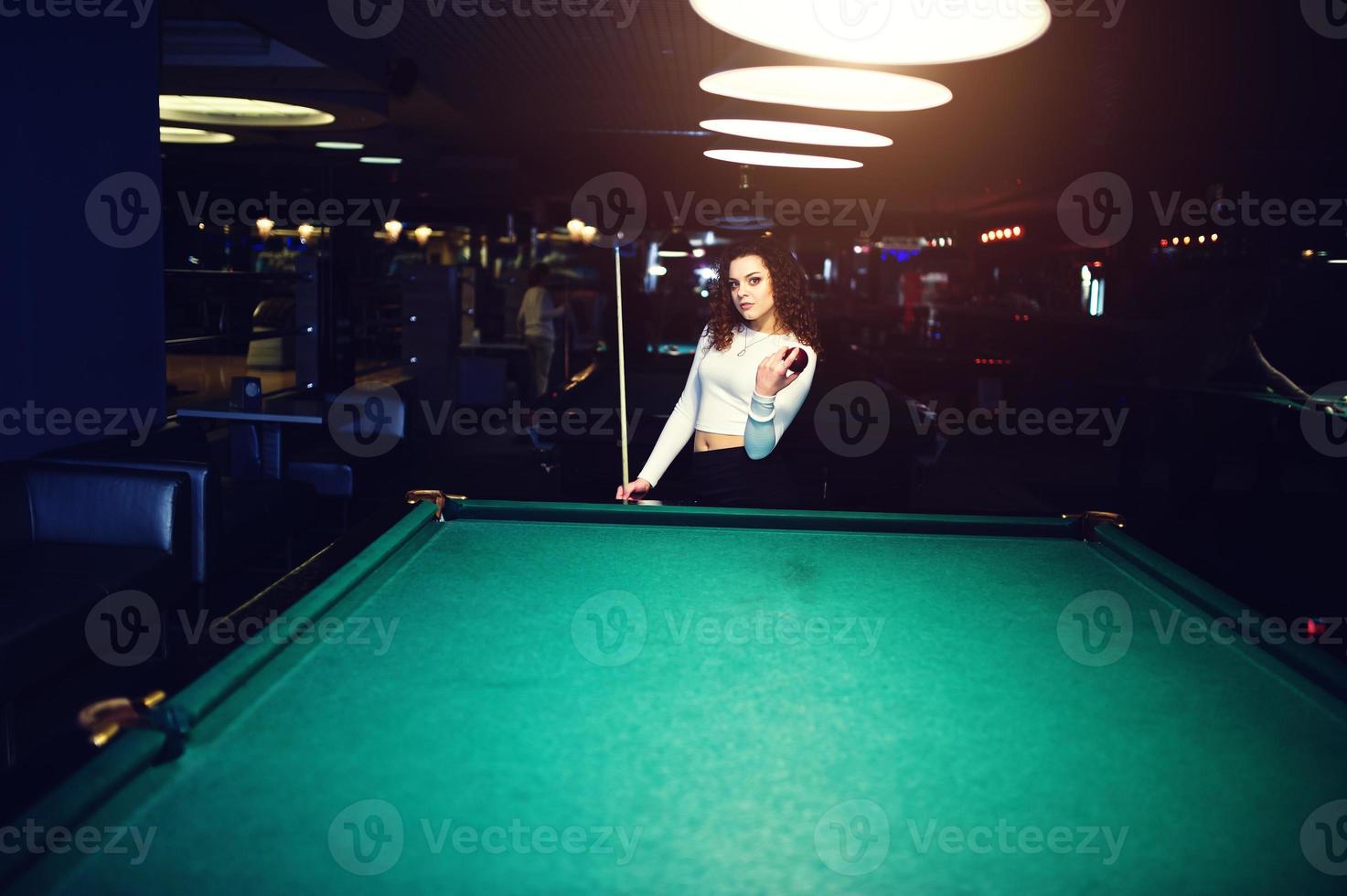 Young curly girl posed near billiard table. Sexy model at black mini mini skirt play russian snooker. Play game and fun concept. photo