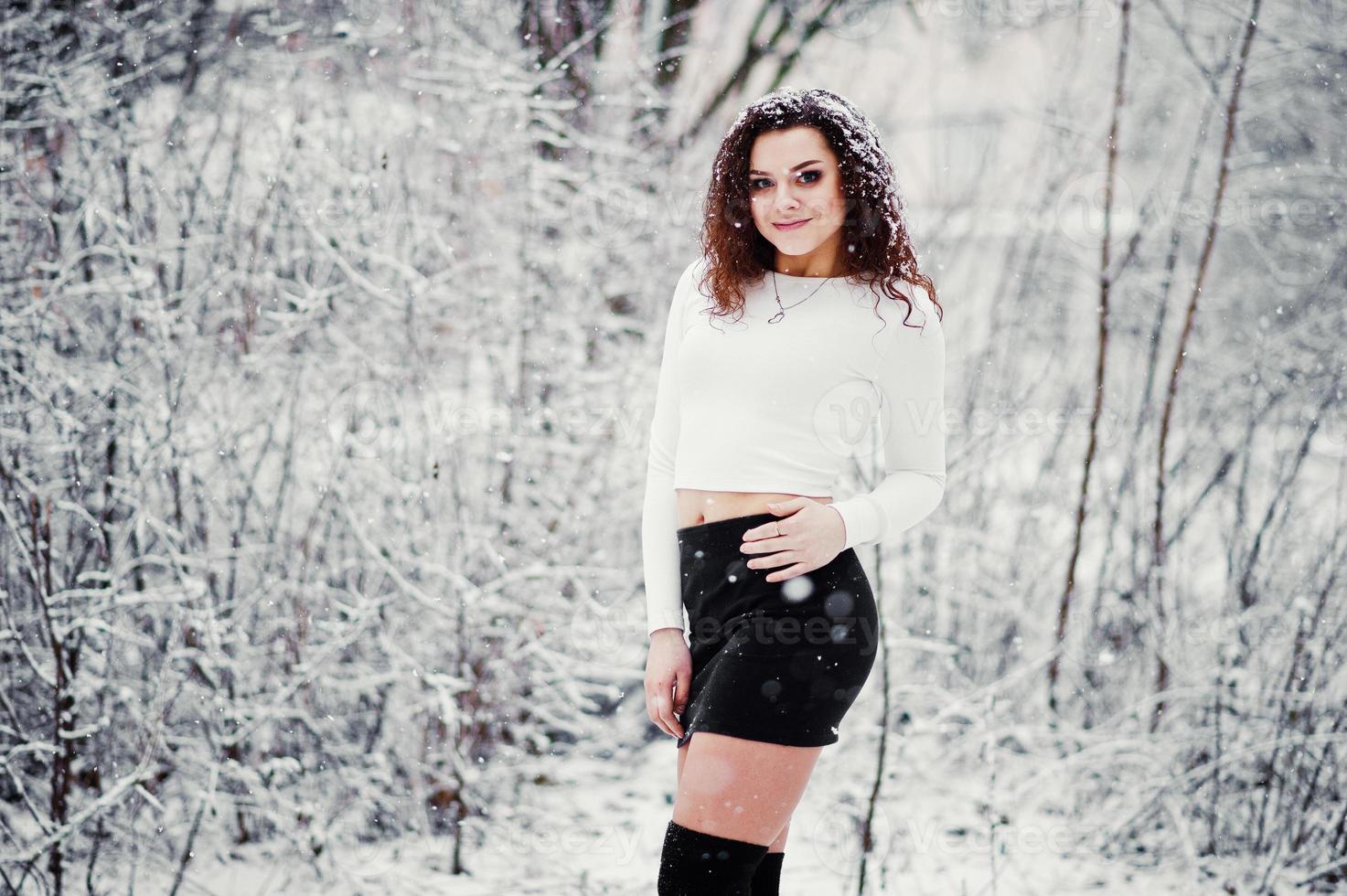 chica morena rizada fondo nieve cayendo, usar minifalda negra y medias de lana. modelo en invierno. retrato de moda en tiempo de nieve. foto en tonos de instagram.