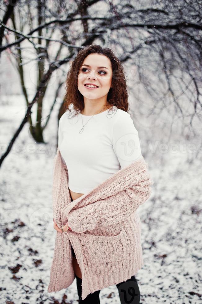 niña morena rizada fondo nieve cayendo, usar suéter de punto cálido, minifalda negra y medias de lana. modelo en invierno. retrato de moda en tiempo de nieve. foto en tonos de instagram.