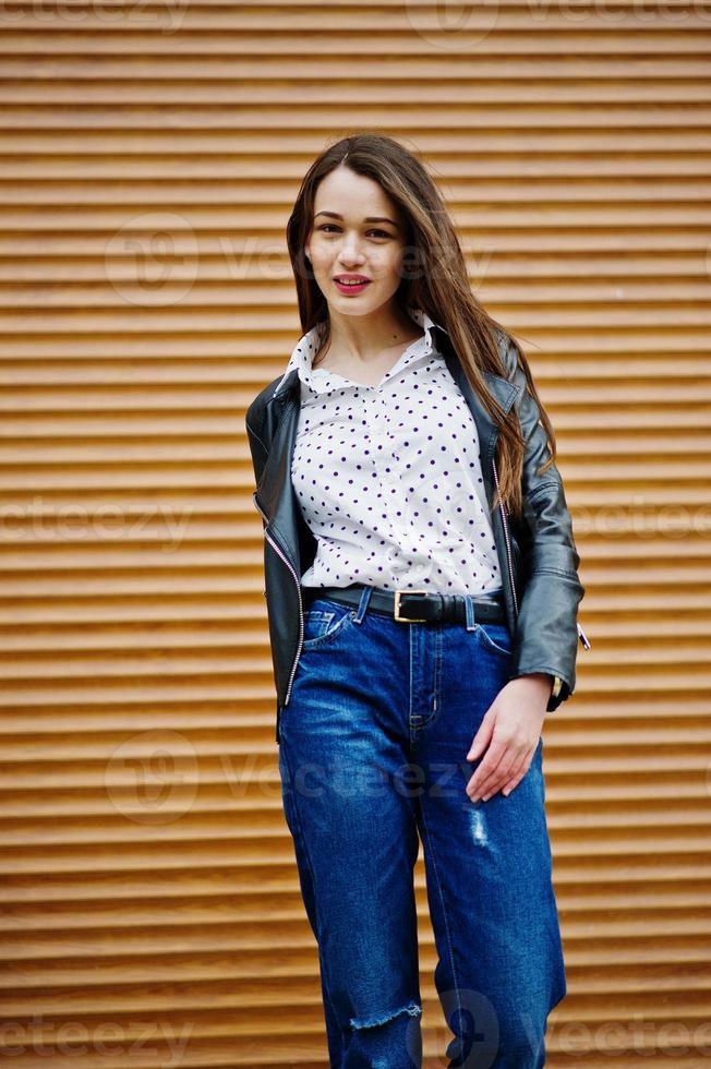 Portrait of stylish young girl wear on leather jacket and ripped jeans background shutter texture. Street fashion model style. photo