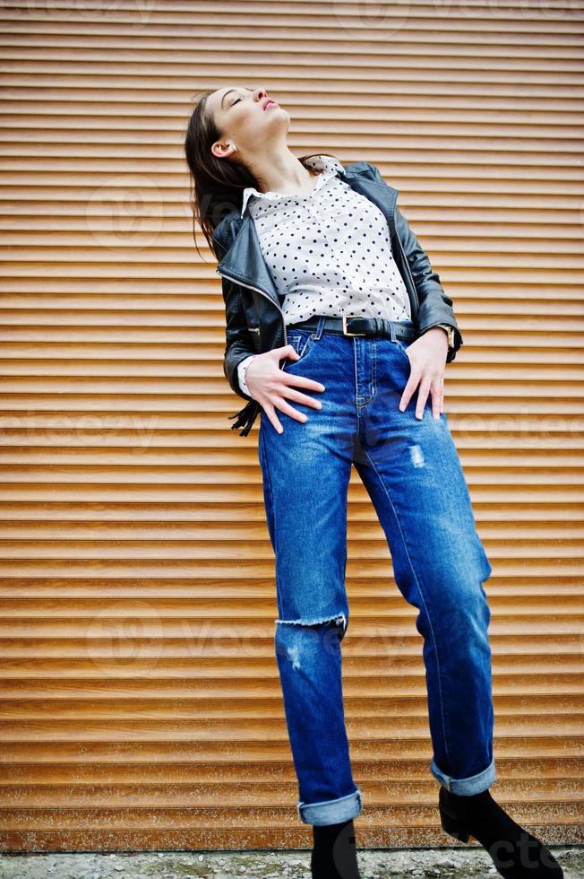 Full length portrait of stylish young girl wear on leather jacket and ripped jeans background shutter texture. Street fashion model style. photo