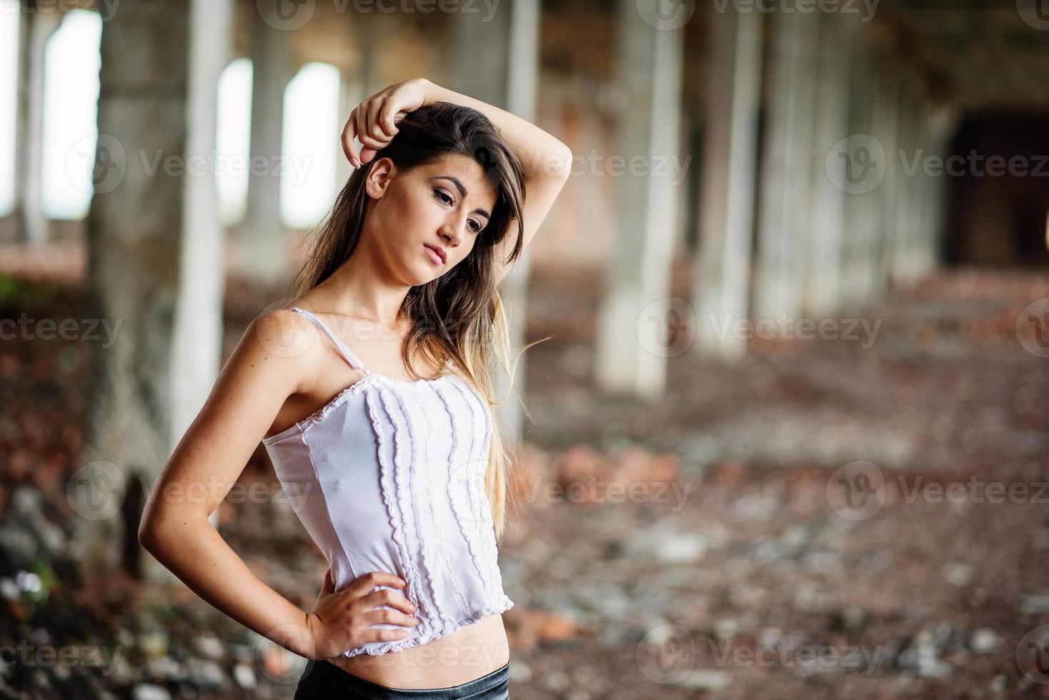 retrato de una joven morena linda con pantalones de cuero negro y blusa blanca posada en un lugar abandonado. foto