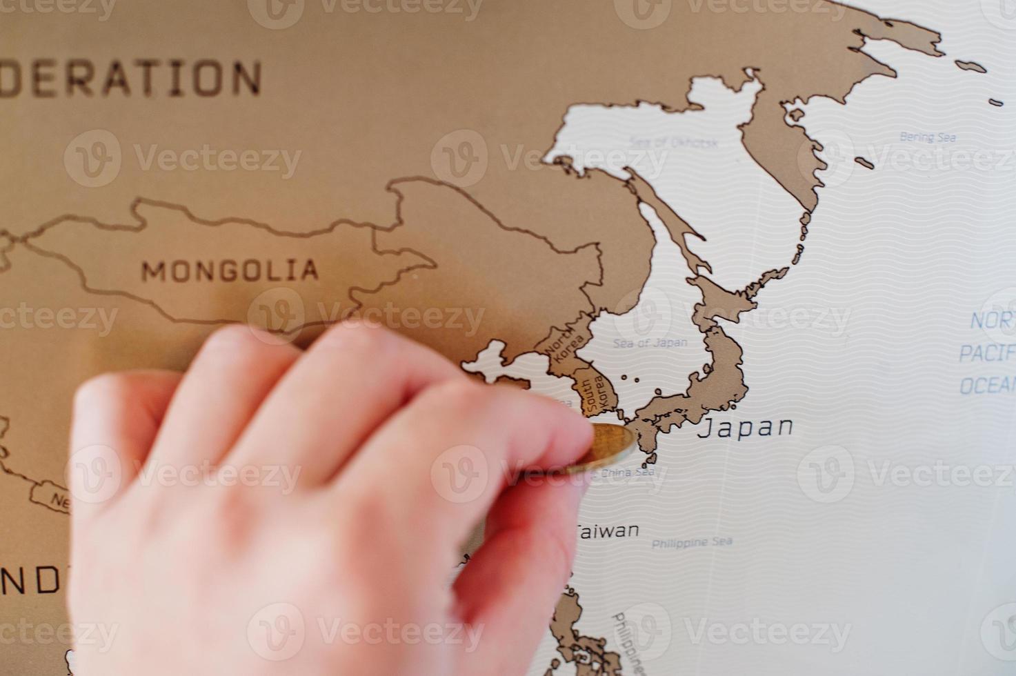 Rascar el mapa de viaje del mundo. la mano del hombre borra Japón con una moneda. foto