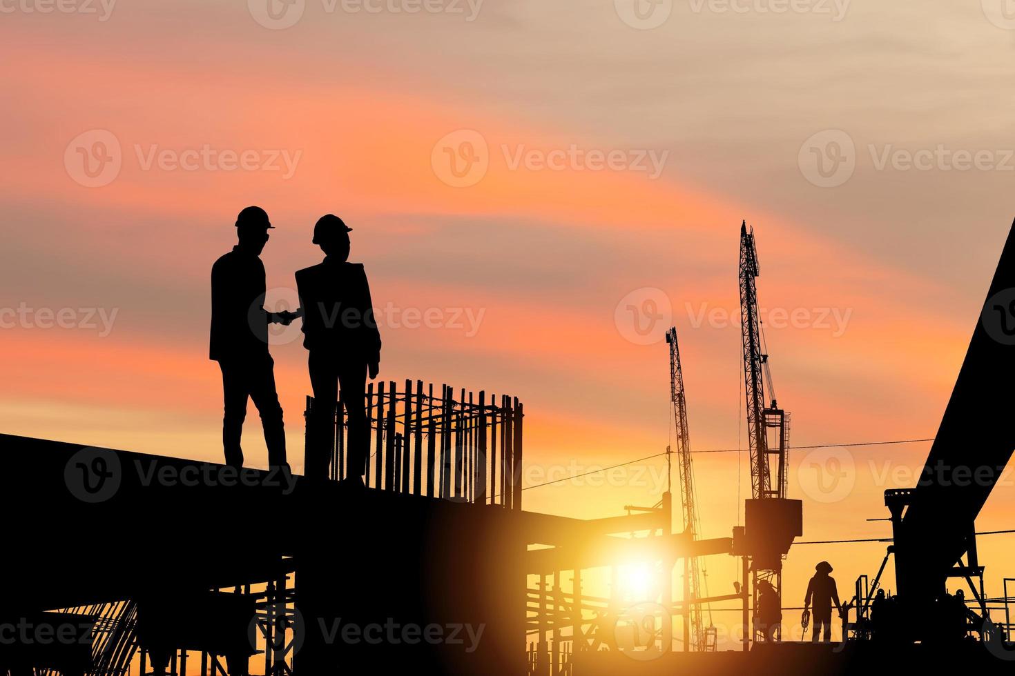 silueta de ingeniero y equipo de trabajadores revisando el proyecto en el fondo del sitio de construcción, construcción de una línea de tren de transporte masivo en progreso con un sitio de infraestructura pesado al atardecer en el tiempo de la tarde foto