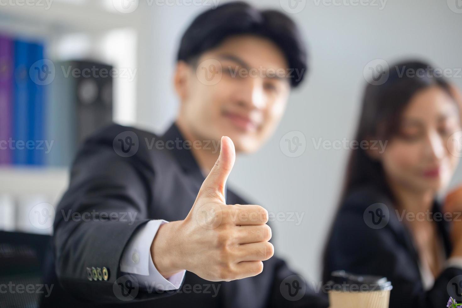 hombre de negocios alegre que muestra los pulgares hacia arriba con un grupo de empresarios reunidos en la oficina foto