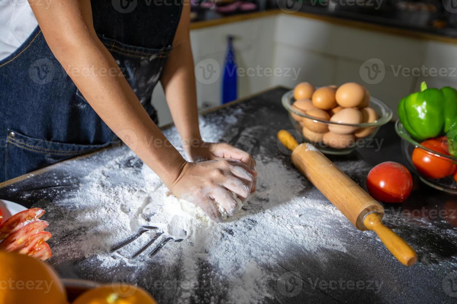 mujeres asiáticas preparando una pizza, amasan la masa y ponen los ingredientes en la mesa de la cocina foto