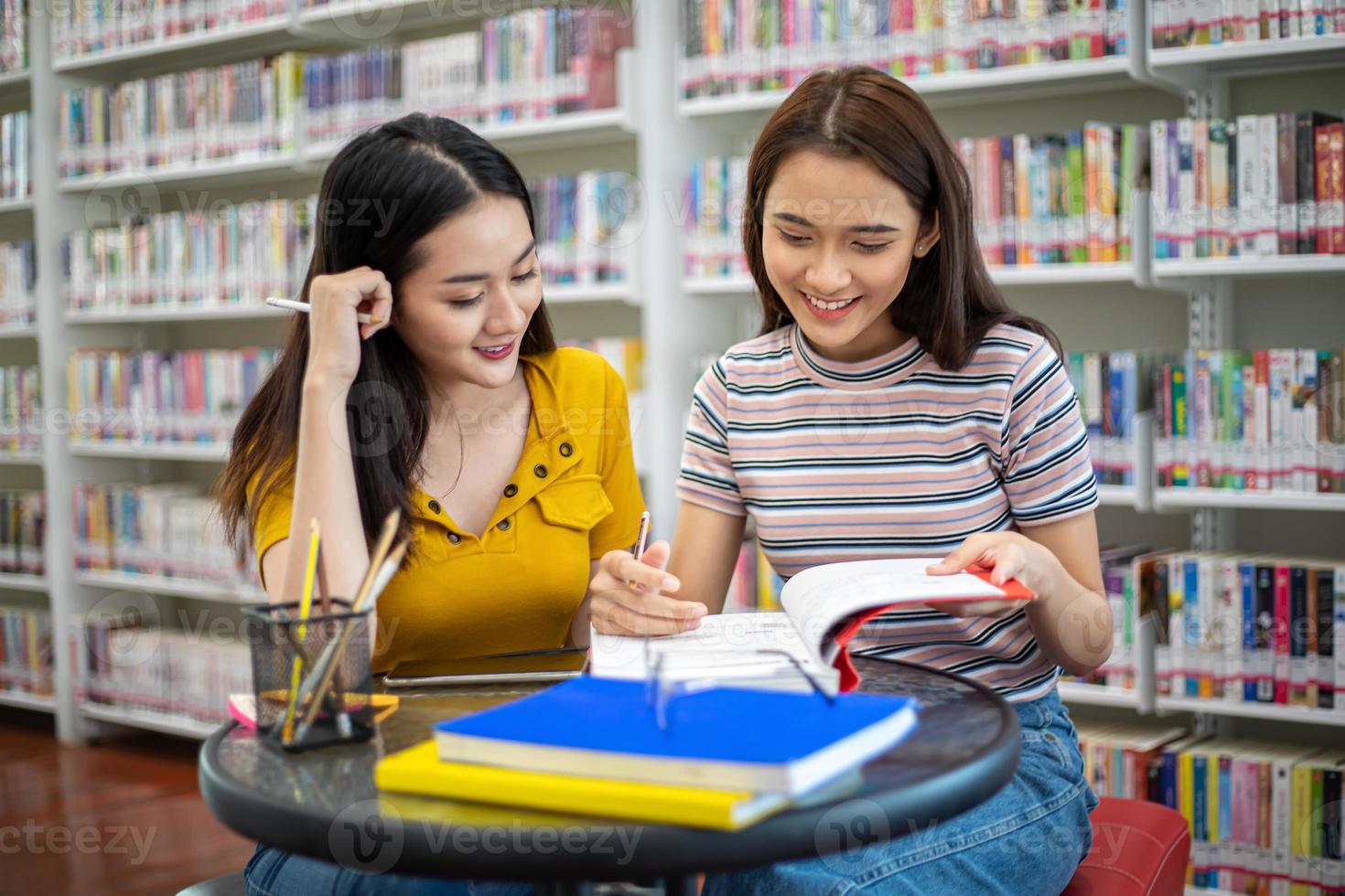 los estudiantes asiáticos del grupo sonríen y leen libros y usan un cuaderno para ayudar a compartir ideas en el trabajo y el proyecto. y también repasar el libro antes del examen foto