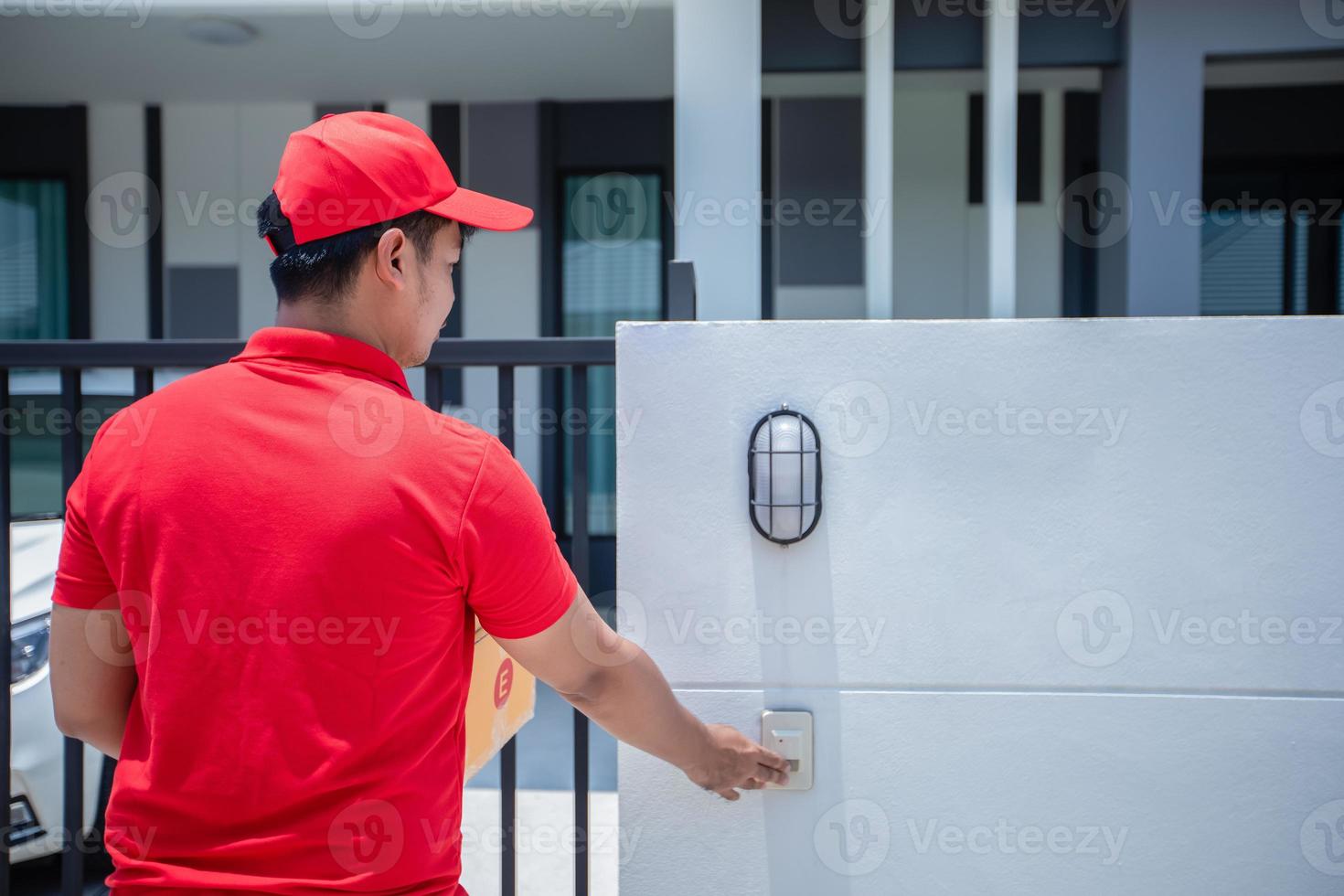 Asian delivery servicemen wearing a red uniform with a red cap handling cardboard boxes to give to the customer in front of the house and Click the doorbell. Online shopping and Express delivery photo