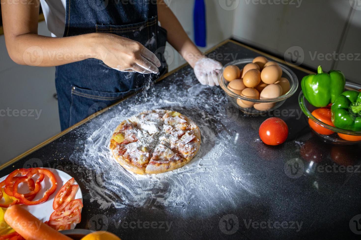 Asian women preparing a pizza, knead the dough and puts ingredients on kitchen table photo