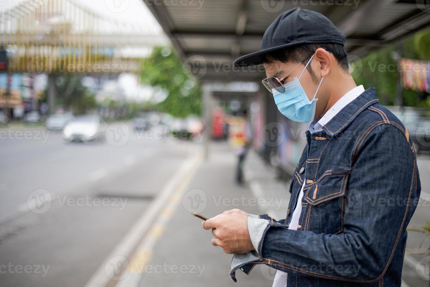 Asian Young man using smart phone in the city and wearing face mask for protection air pollution, particulates and for protection flu virus, influenza, coronavirus photo