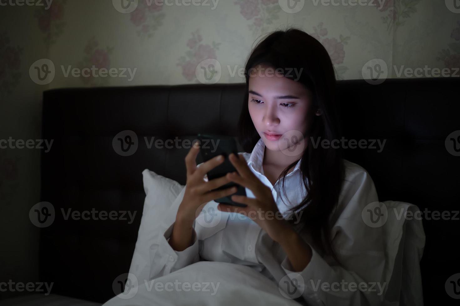 Asian woman using a mobile phone on night at the bed.She smiles and enjoys at home. photo