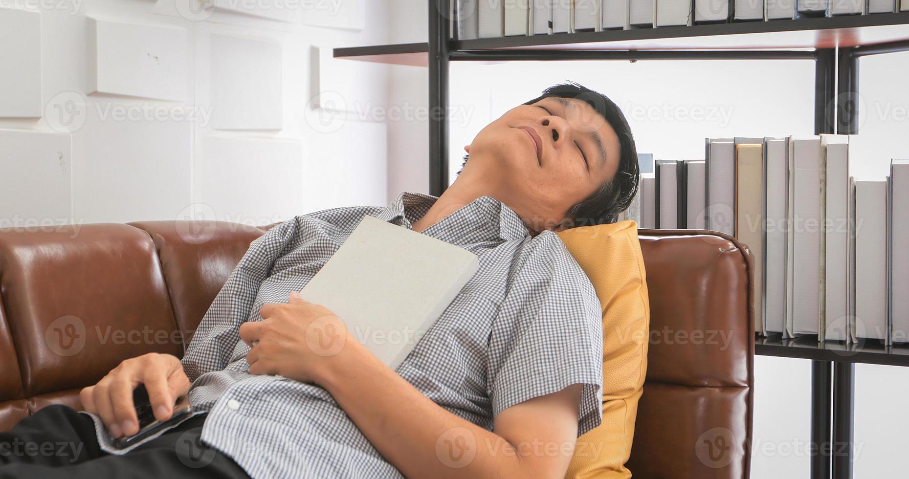 un anciano asiático leyendo un libro y durmiendo en un sofá en la sala de estar en casa, el retrato de un anciano asiático es relajante y feliz con leer una revista foto