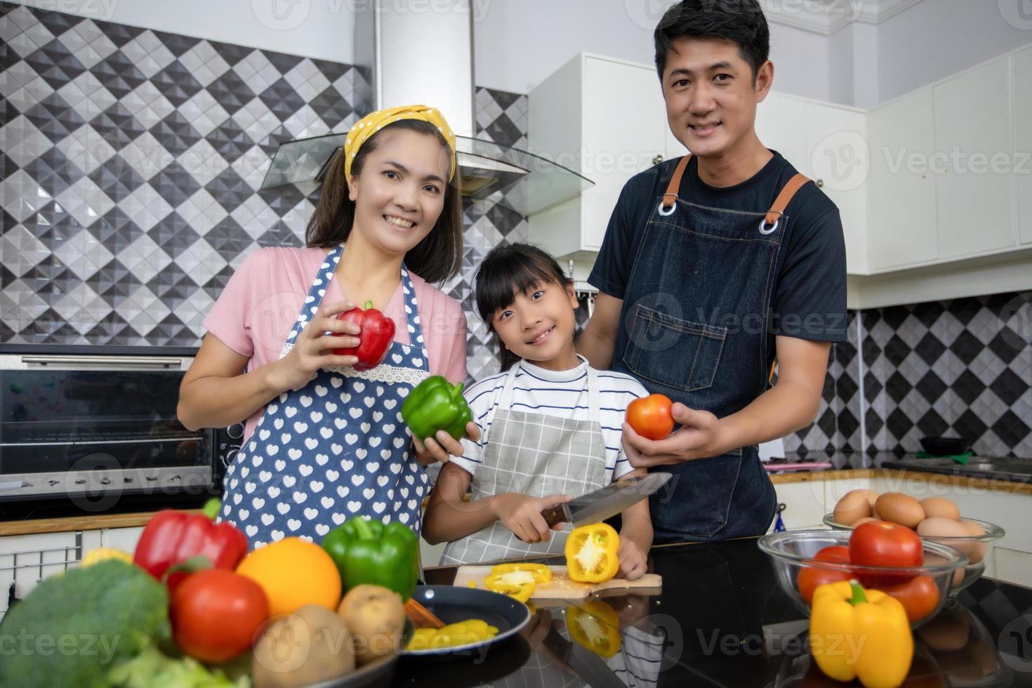 familia feliz tiene a papá, mamá y su pequeña hija cocinando juntos en la cocina foto